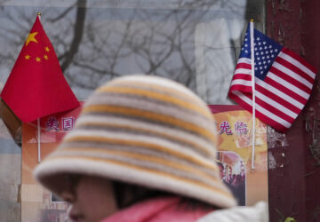 A woman walks by the Chinese and U.S. national flags on display outside a souvenir shop in Beijing on Jan. 31, 2025. (AP Photo/Andy Wong)