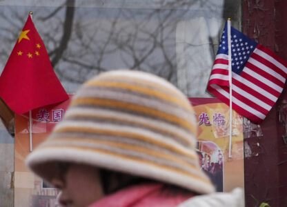 A woman walks by the Chinese and U.S. national flags on display outside a souvenir shop in Beijing on Jan. 31, 2025. (AP Photo/Andy Wong)