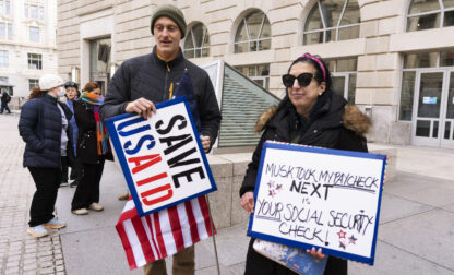 Priya Kathpal, right, and Taylor Williamson, left, who work for a company doing contract work for the United States Agency for International Development, or USAID, carry signs outside the USAID headquarters in Washington, Monday, Feb. 10, 2025. (AP Photo/Manuel Balce Ceneta)