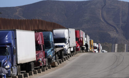 Trucks line up to cross the border into the United States as tariffs against Mexico go into effect, Tuesday, March 4, 2025, in Tijuana, Mexico. (AP Photo/Gregory Bull)