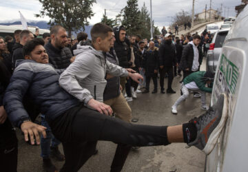 People hit a car on its side while protesting near the home of the owner of a nightclub that was the scene of a massive fire, after a vigil for the victims in the town of Kocani, North Macedonia, Monday, March 17, 2025. (AP Photo/Visar Kryeziu)