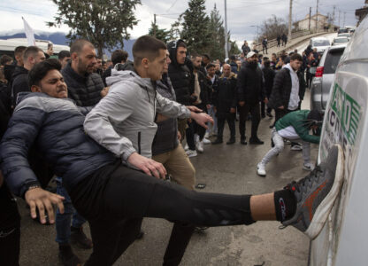 People hit a car on its side while protesting near the home of the owner of a nightclub that was the scene of a massive fire, after a vigil for the victims in the town of Kocani, North Macedonia, Monday, March 17, 2025. (AP Photo/Visar Kryeziu)