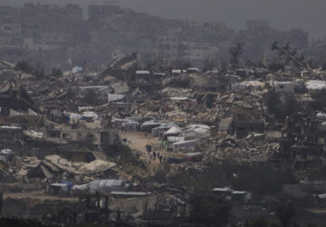 People walking surrounded by buildings destroyed during the Israeli air and ground offensive in the Gaza Strip are seen from southern Israel, Thursday, March 20, 2025. (AP Photo/Leo Correa)