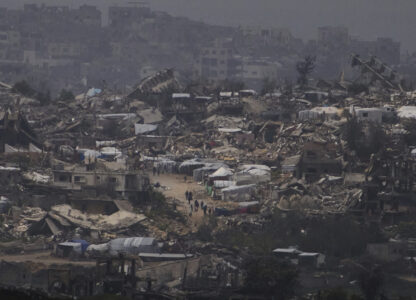 People walking surrounded by buildings destroyed during the Israeli air and ground offensive in the Gaza Strip are seen from southern Israel, Thursday, March 20, 2025. (AP Photo/Leo Correa)